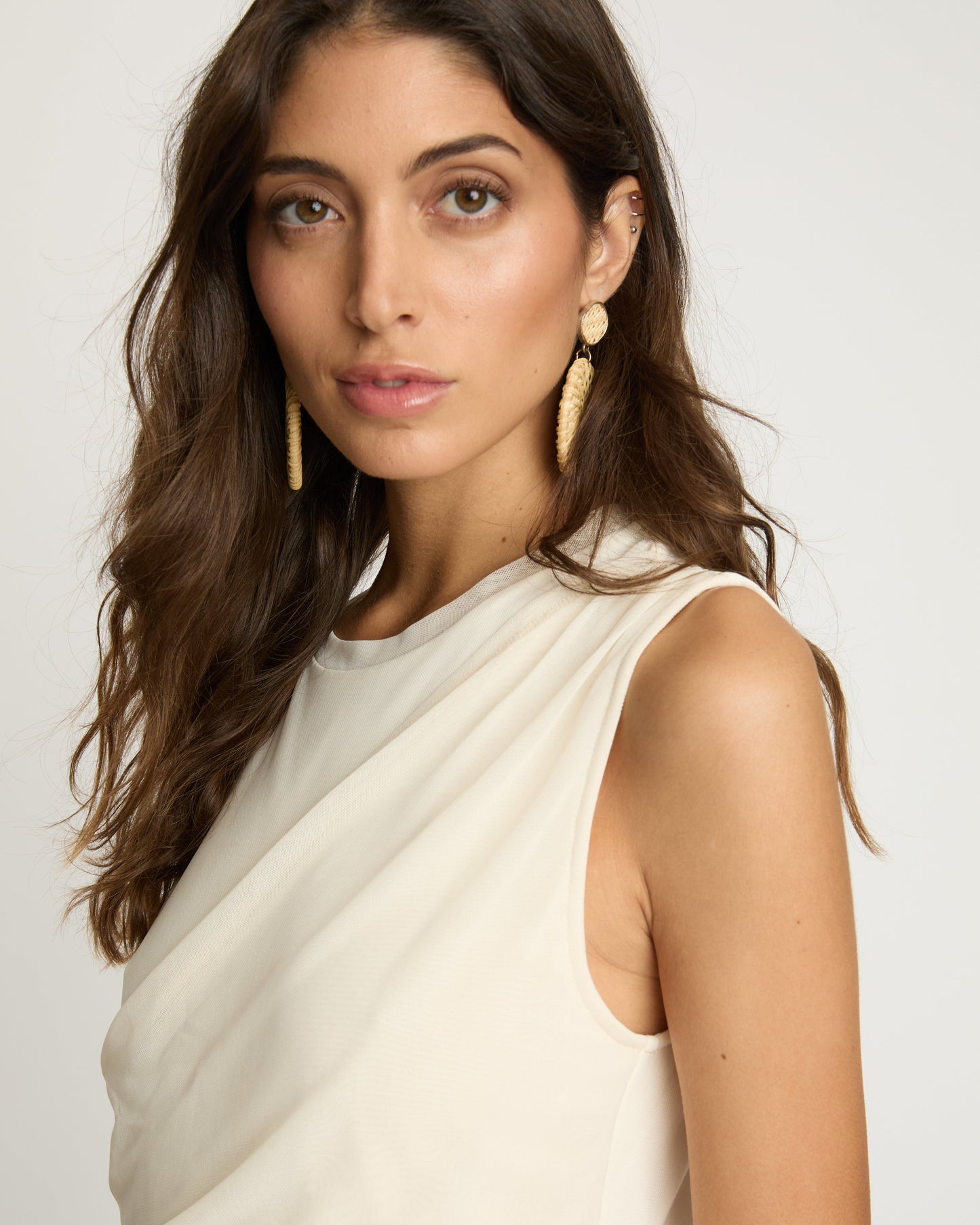Woman wearing a white saree with gold earrings on a plain background