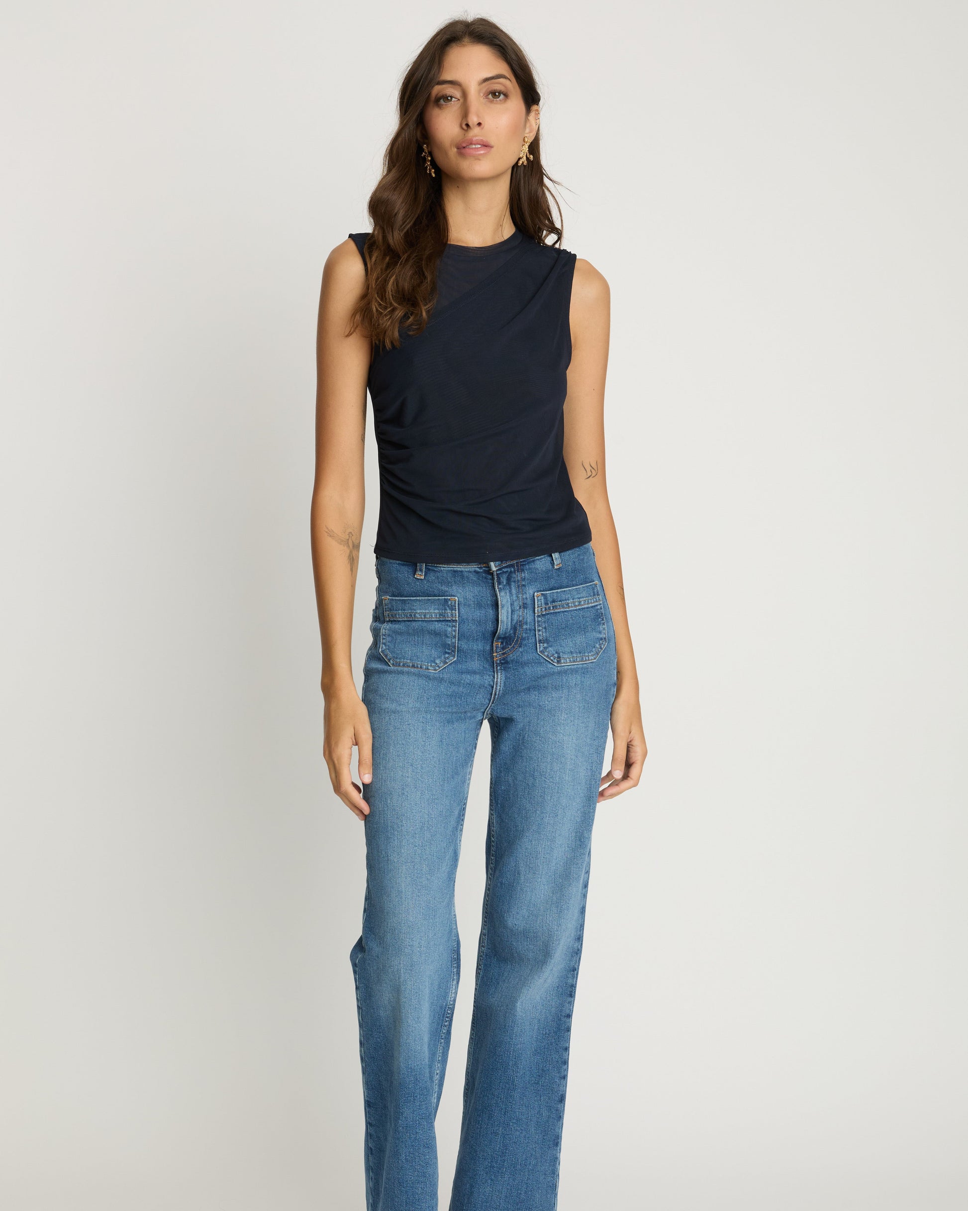 Woman wearing a black sleeveless top and blue jeans on a white background