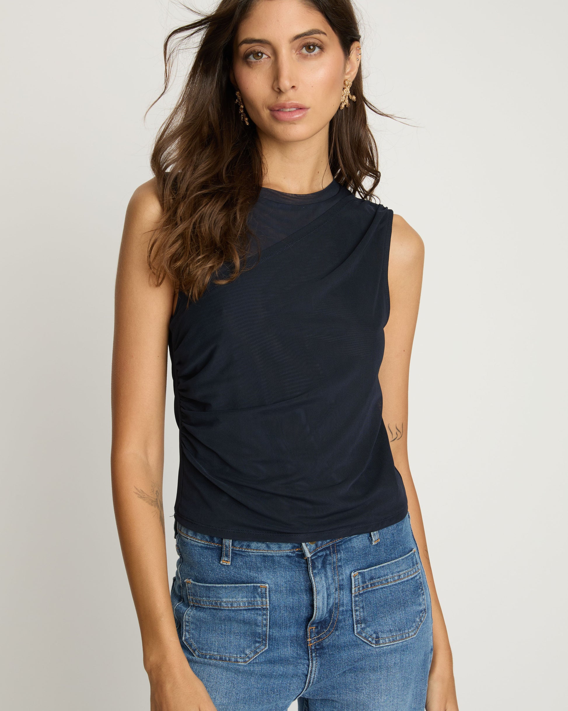 Woman wearing a navy sleeveless top and blue jeans on a plain background