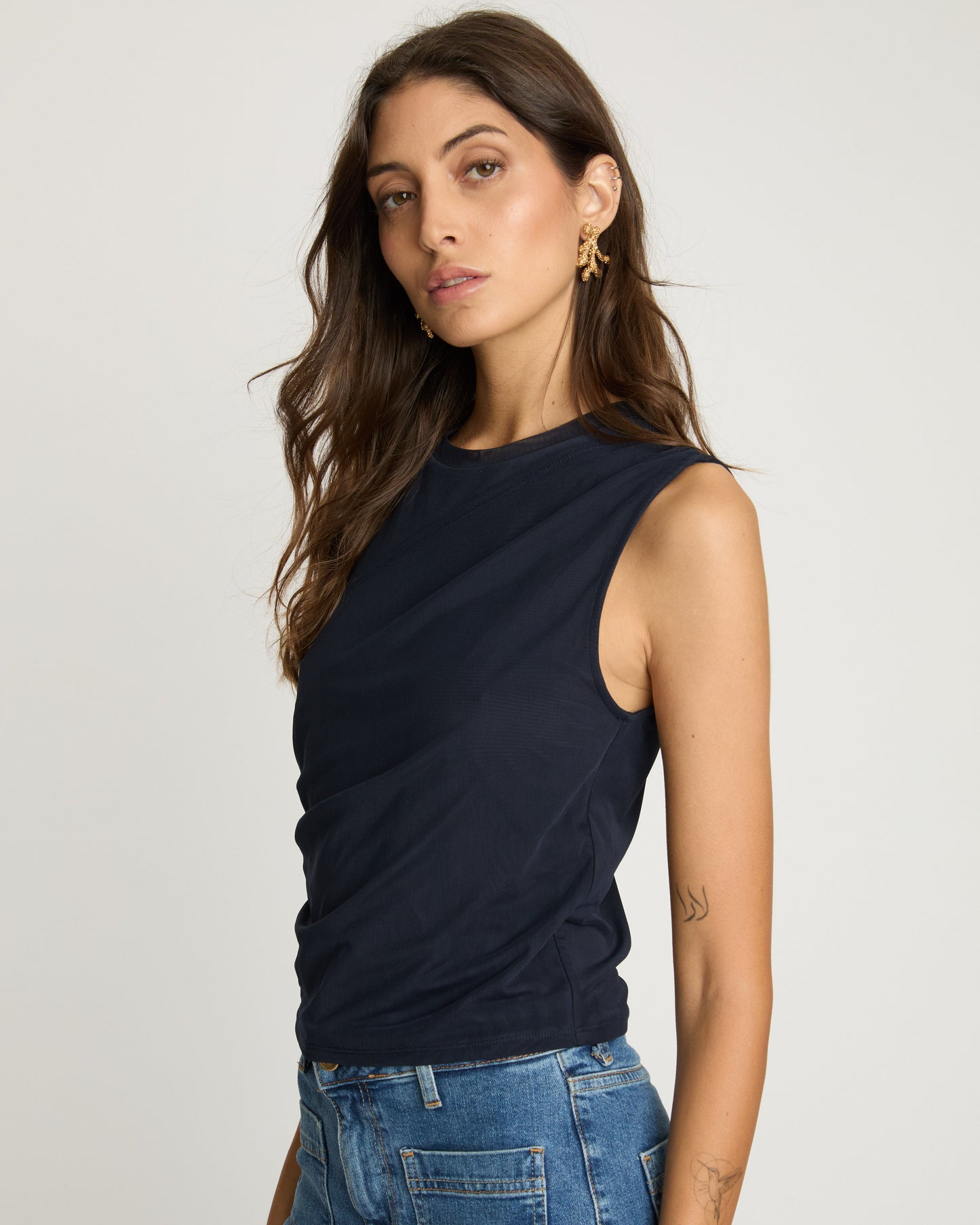 Woman wearing a black sleeveless top and blue jeans against a plain background