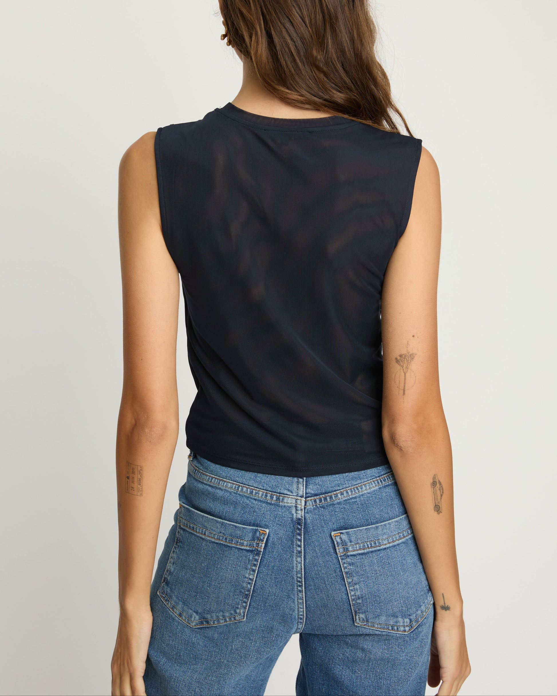 Person wearing a black sleeveless top and blue jeans on a plain background