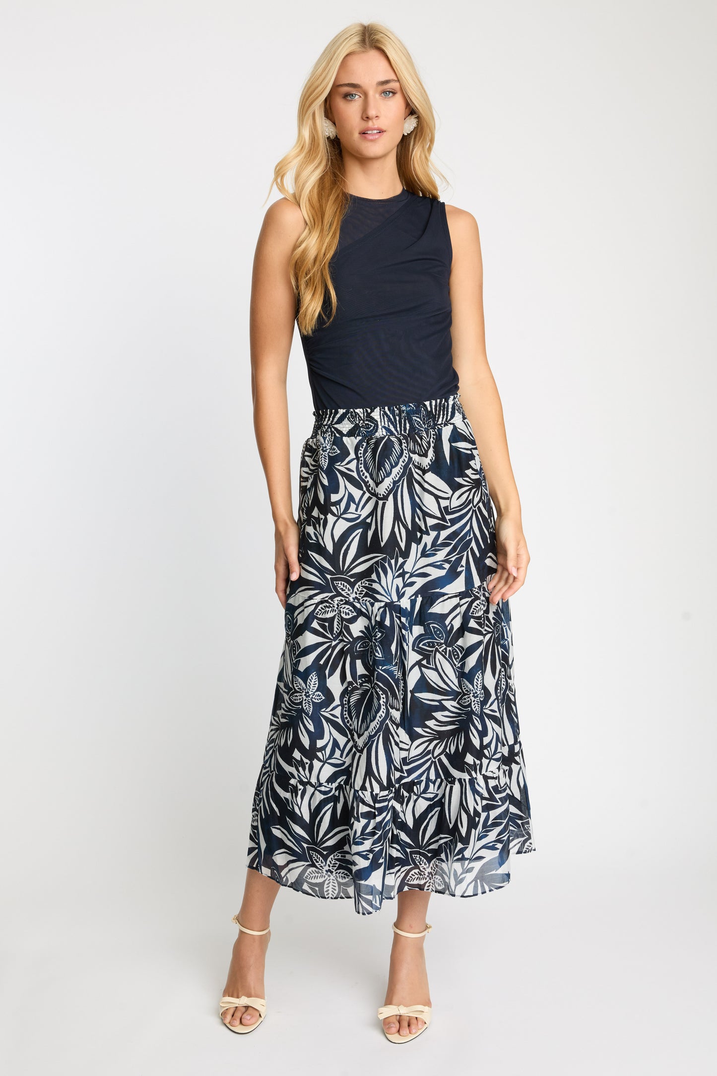 Woman wearing a black sleeveless top and leaf-patterned skirt on a white background