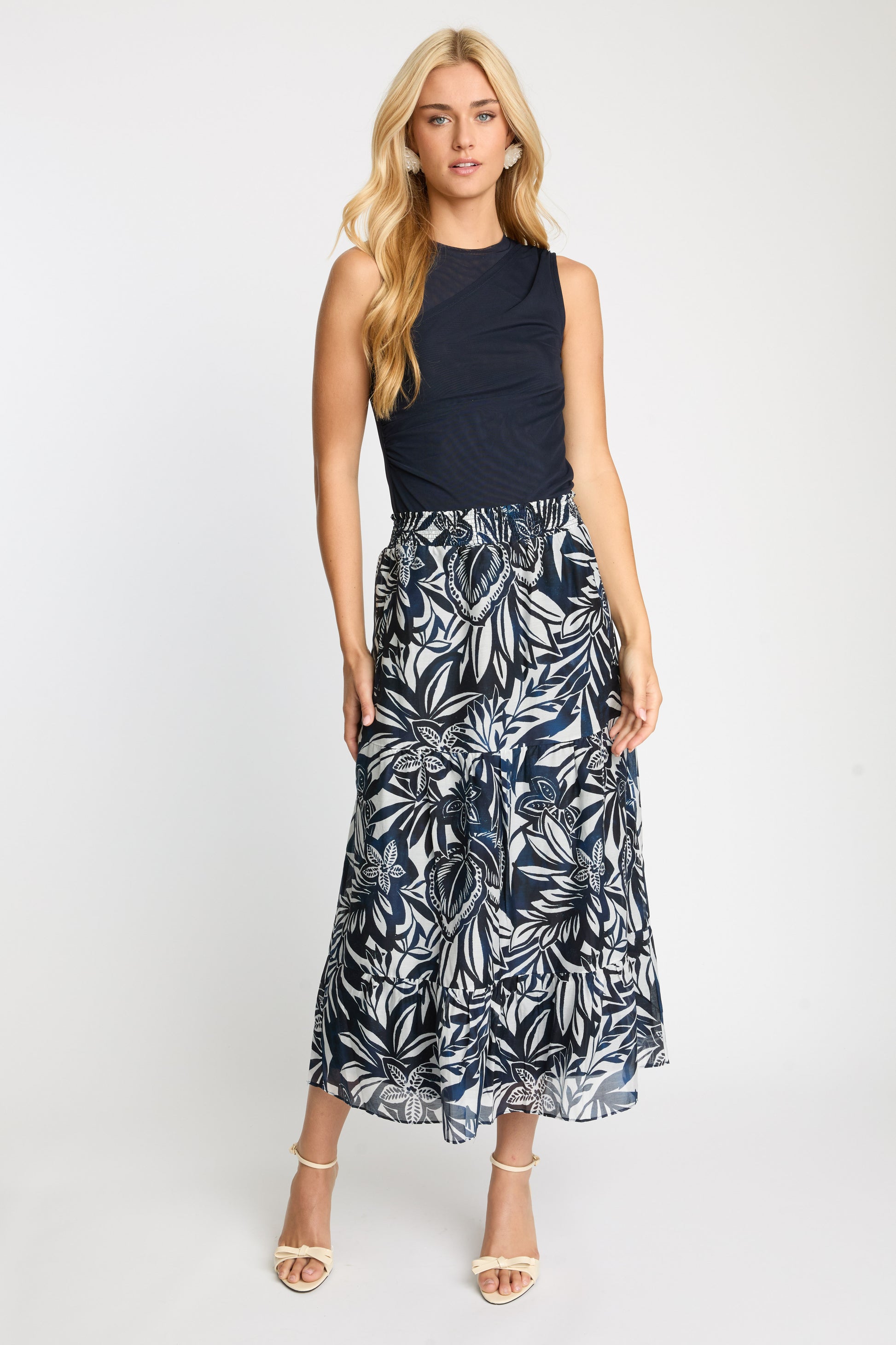 Woman wearing a black sleeveless top and leaf-patterned skirt on a white background