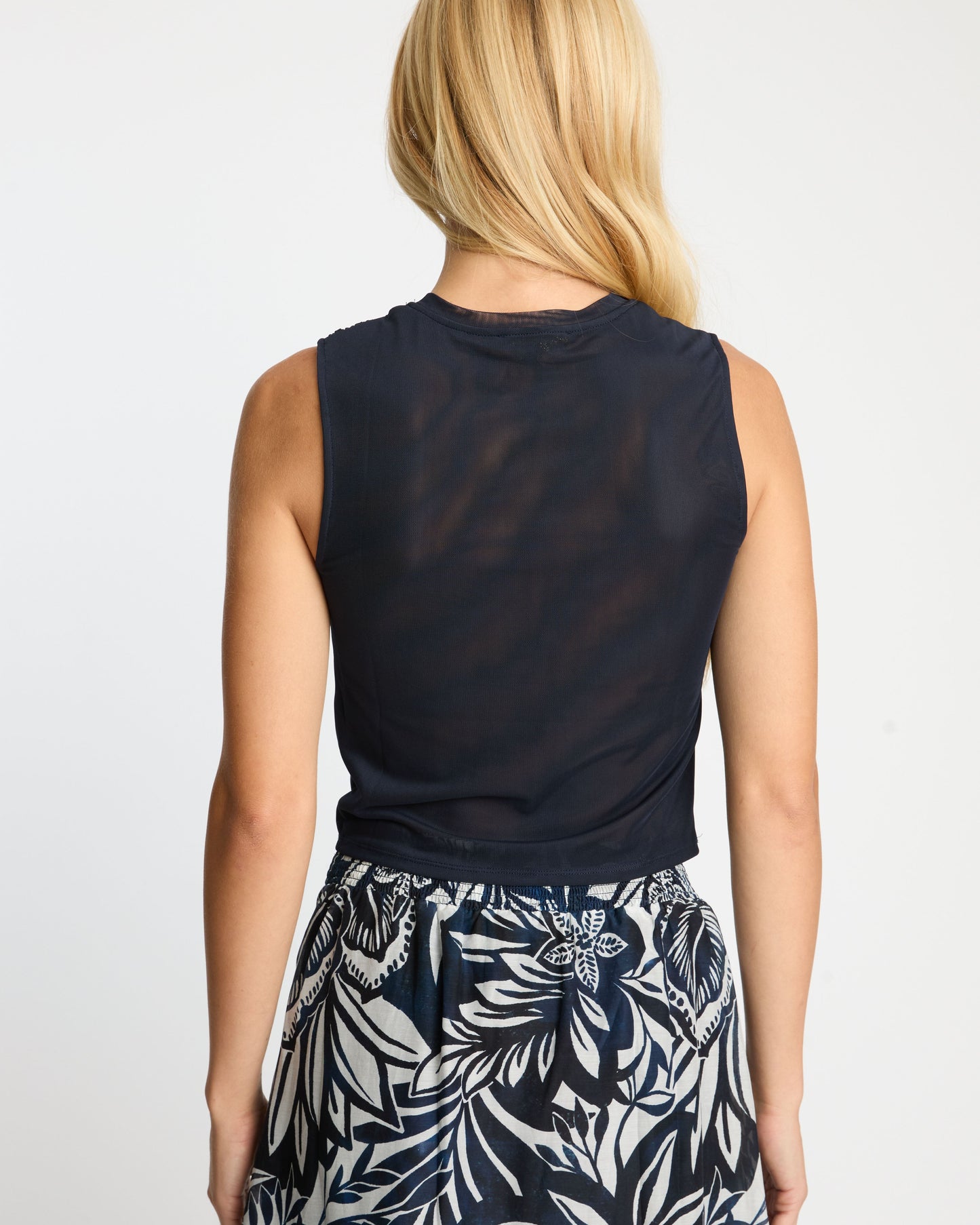 Person wearing a navy sleeveless top and a black and white floral skirt on a plain background