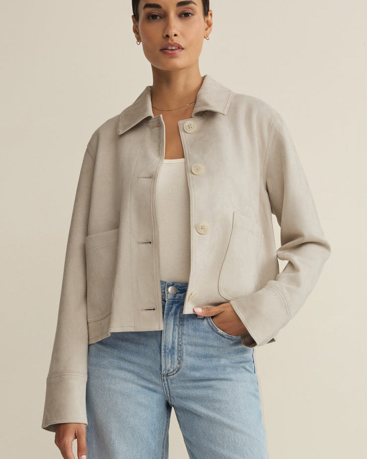 Woman wearing a beige jacket and light blue jeans against a plain background