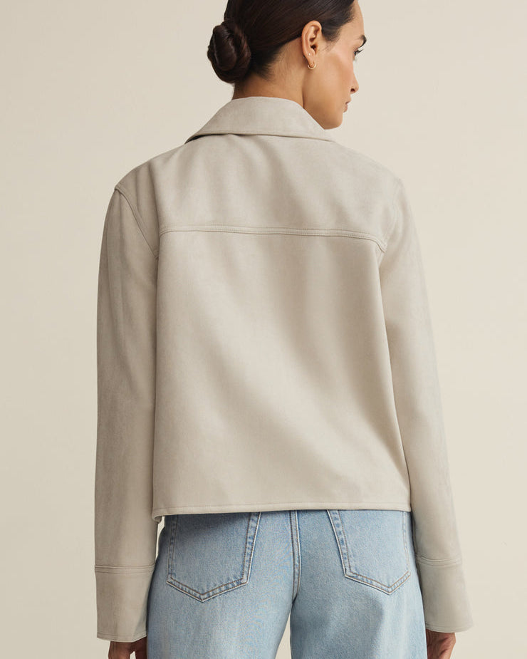 Person wearing a beige jacket and light blue jeans on a plain background