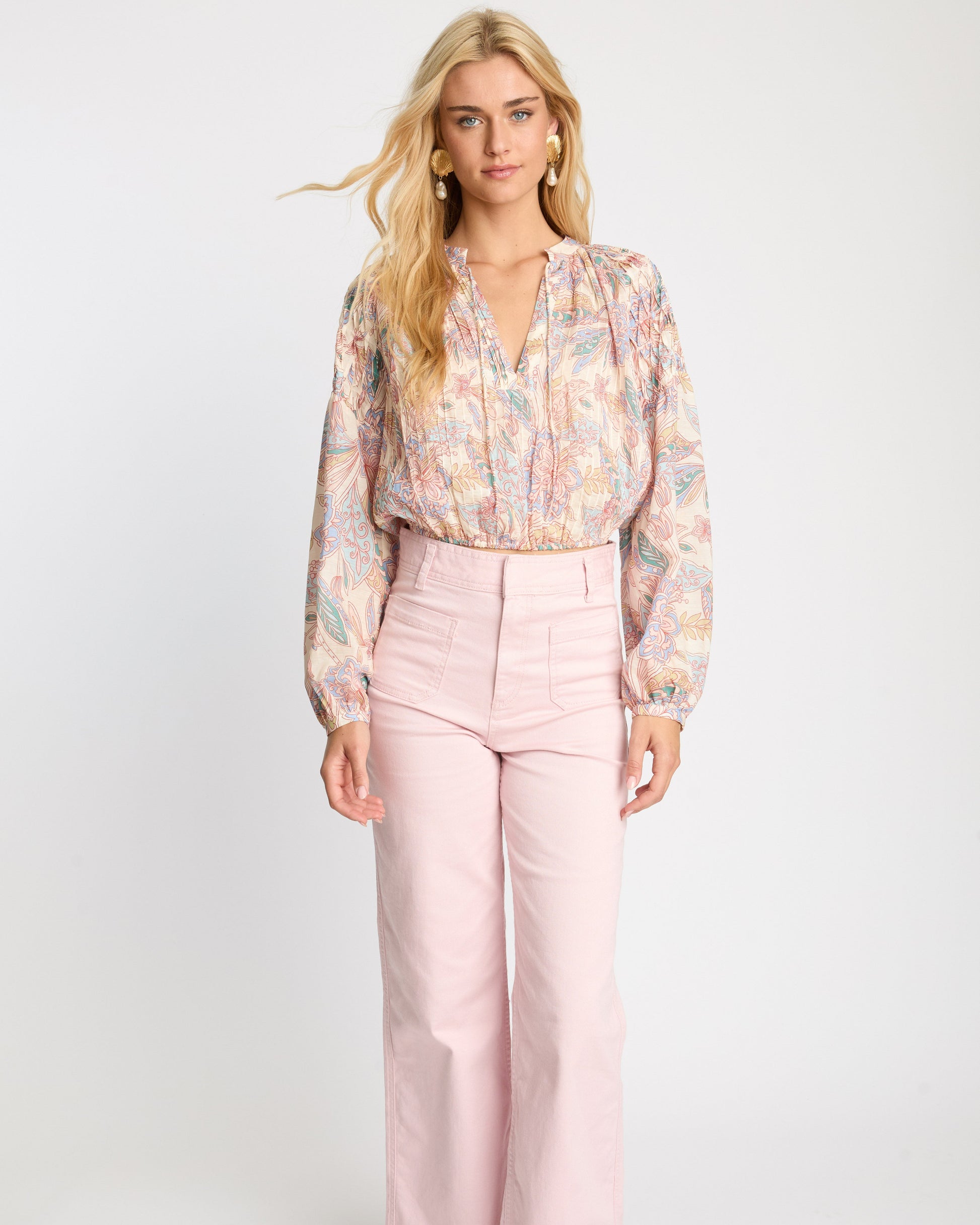 Woman wearing a floral blouse and pink pants on a white background