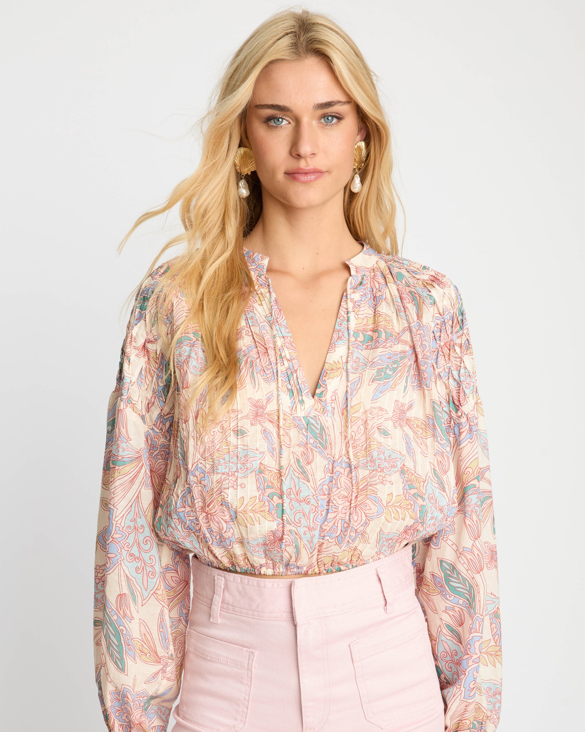 Woman wearing a floral blouse and pink pants on a white background