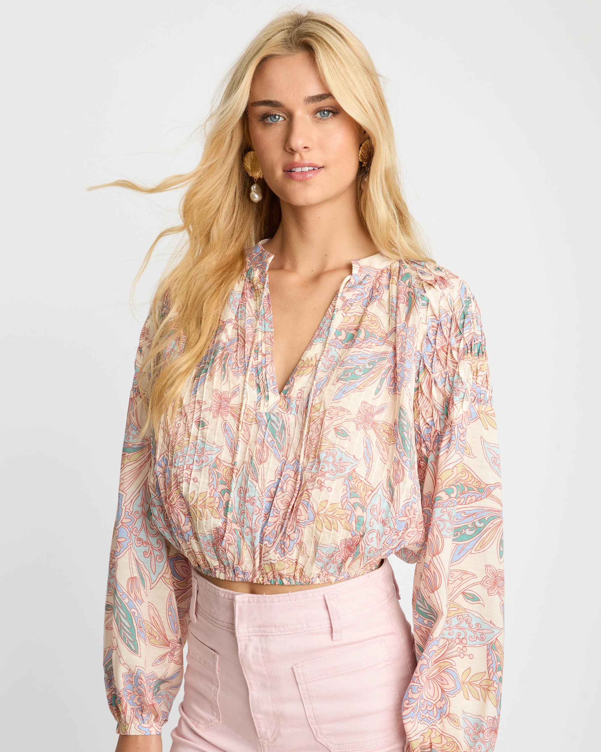 Woman wearing a patterned blouse and pink pants on a white background