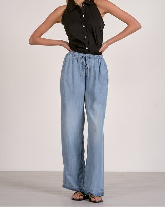 Woman wearing a black sleeveless top and light blue wide-leg jeans against a white background