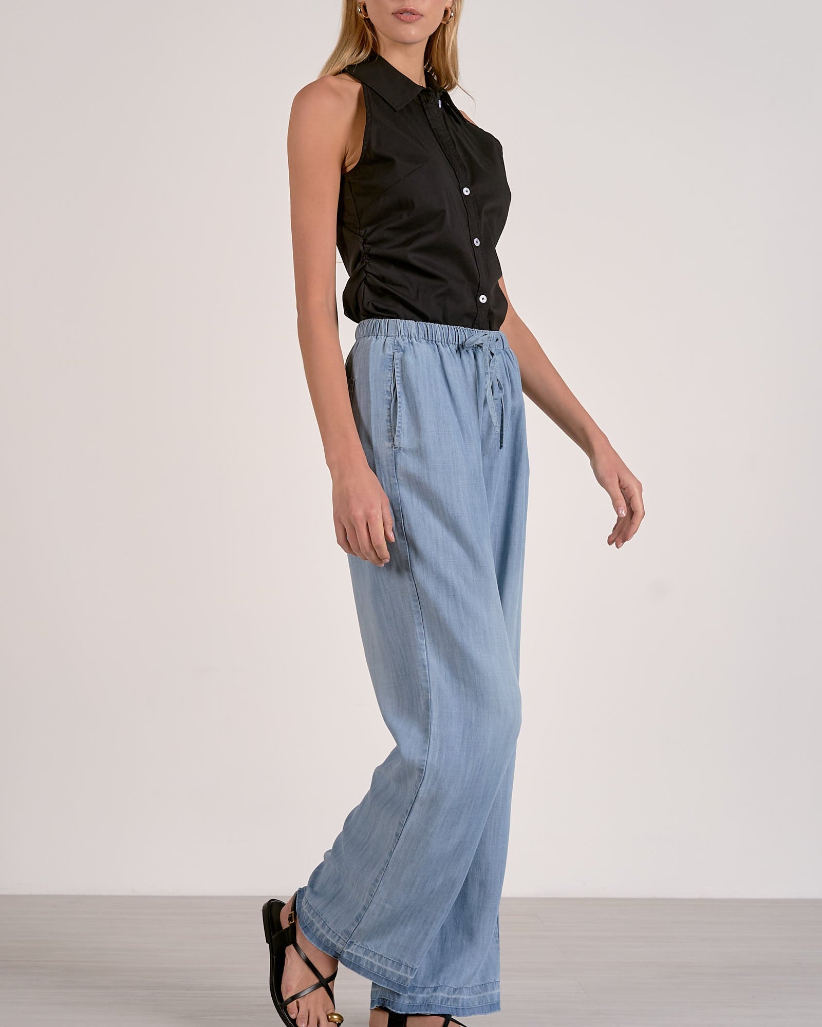 Woman wearing a black sleeveless top and light blue wide-leg pants on a white background