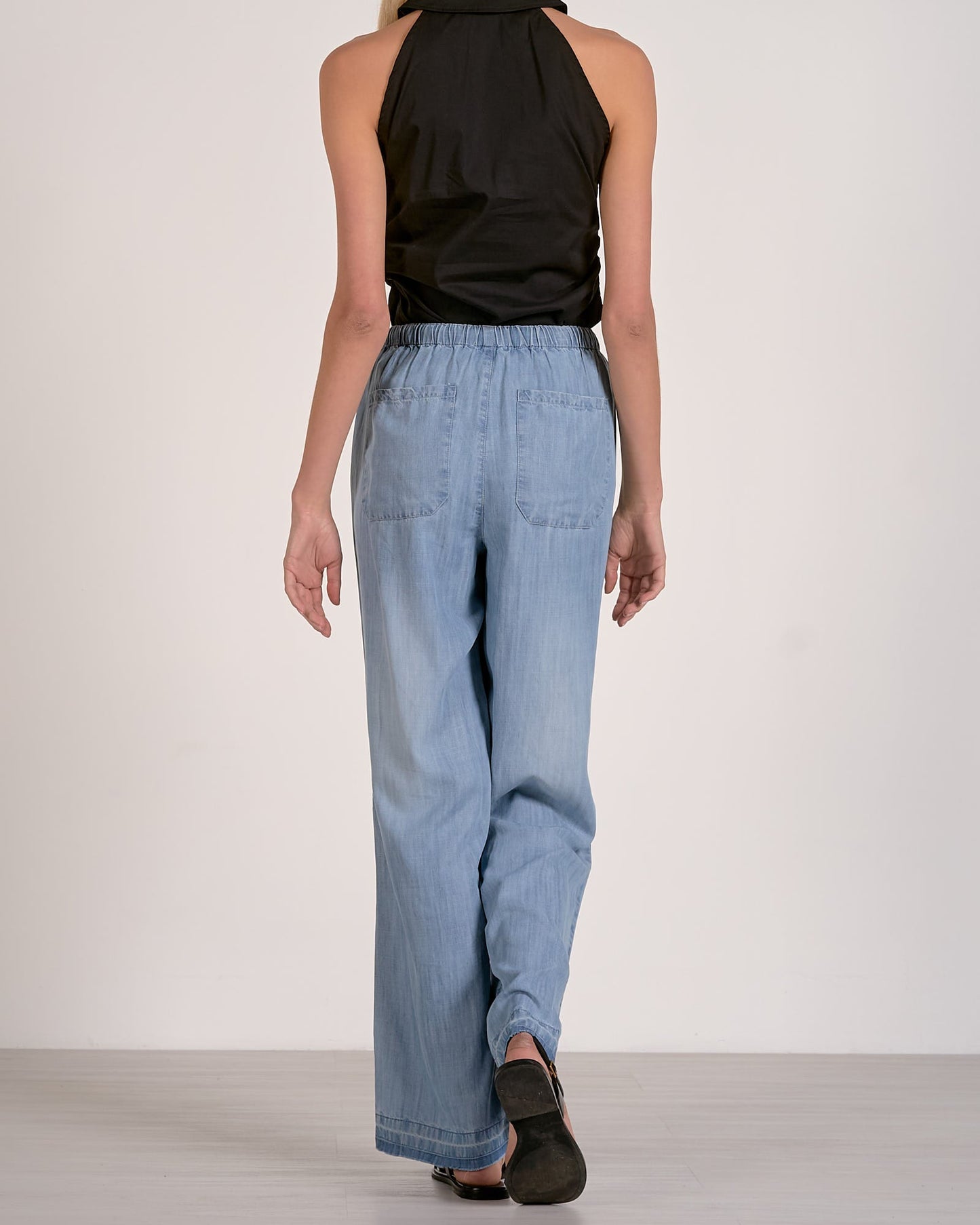 Woman wearing a black sleeveless top and light blue jeans on a white background