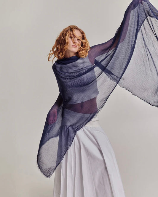 Woman holding a large purple scarf against a plain background