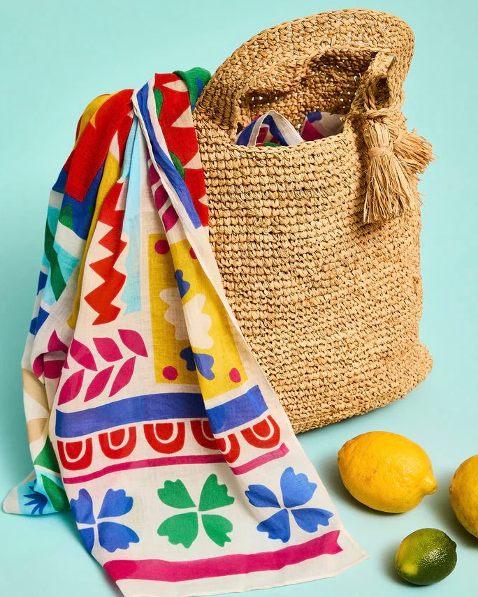 Colorful patterned towel draped over a straw bag with lemons on a light blue background