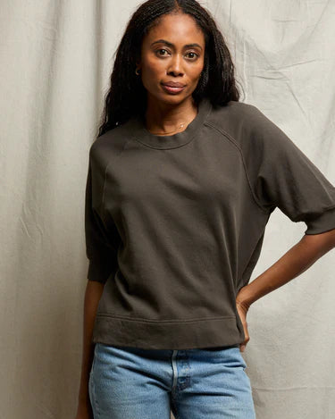 Woman wearing a dark brown sweater and blue jeans against a plain background