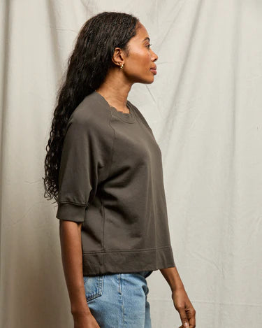 Person wearing a brown sweatshirt and blue jeans against a neutral background