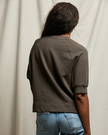 Person wearing a brown jacket and blue jeans against a neutral background