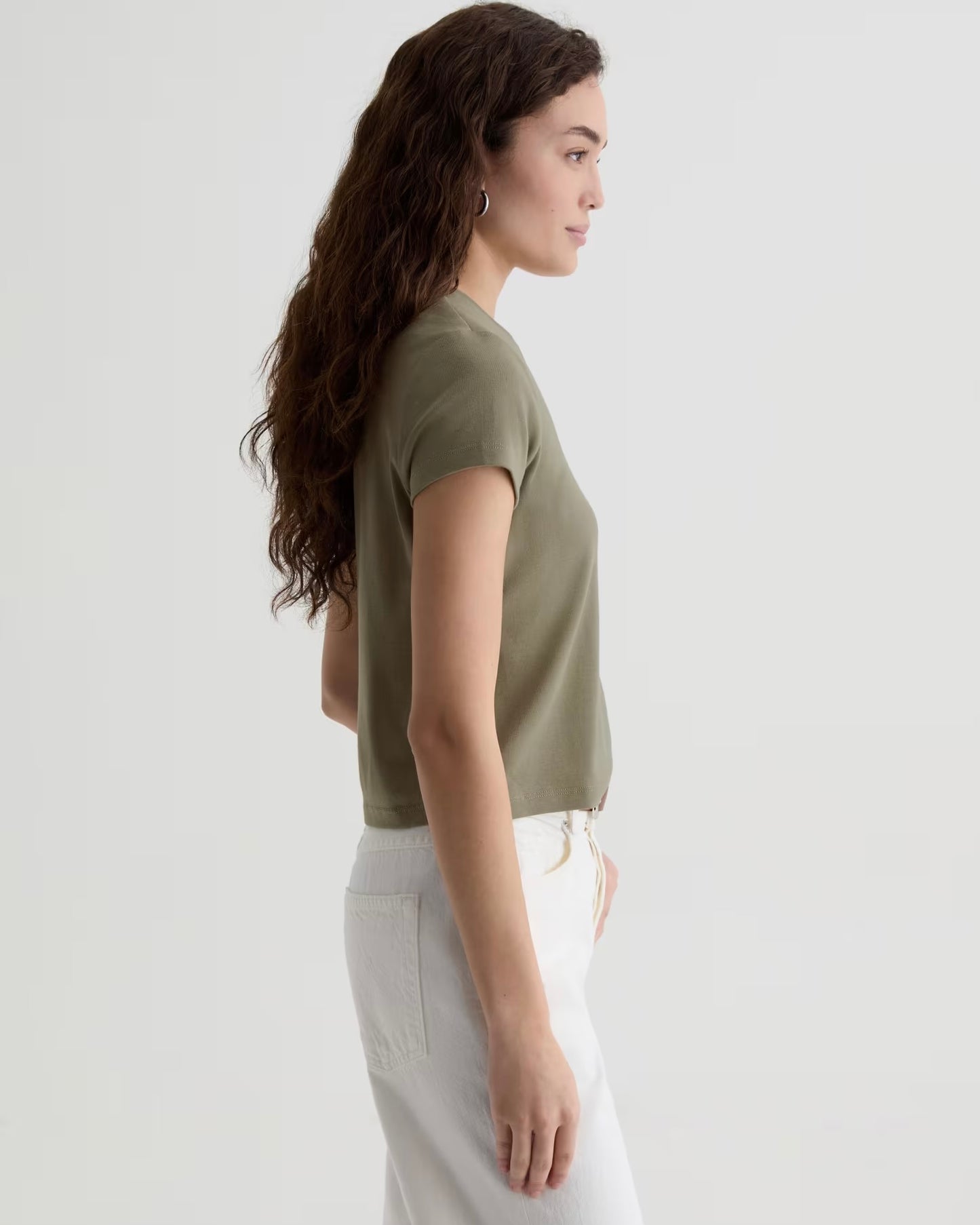 Woman wearing a green top and white pants on a plain background