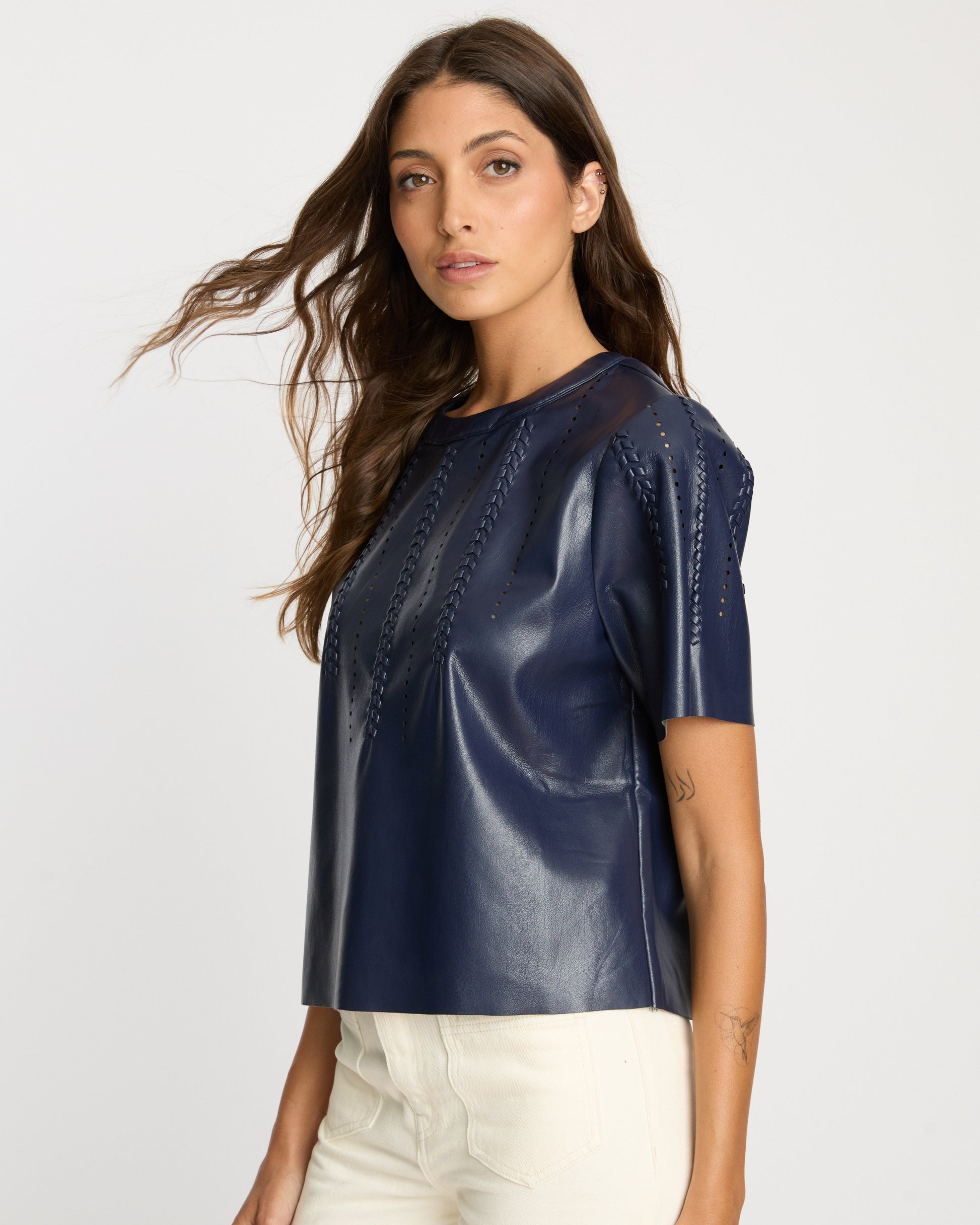 Woman wearing a navy blue leather top with white pants on a light gray background