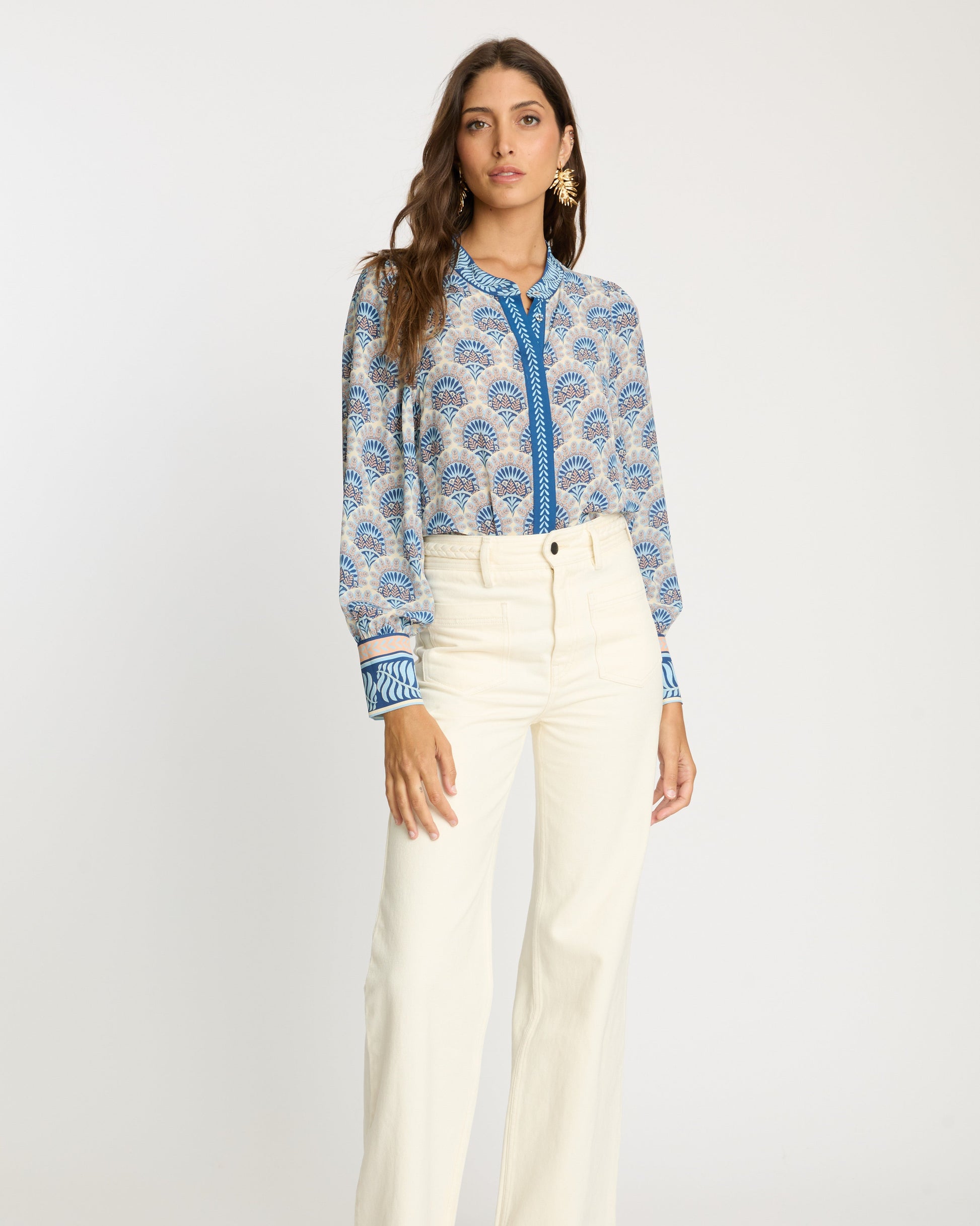 Woman wearing a blue patterned blouse and white pants on a white background