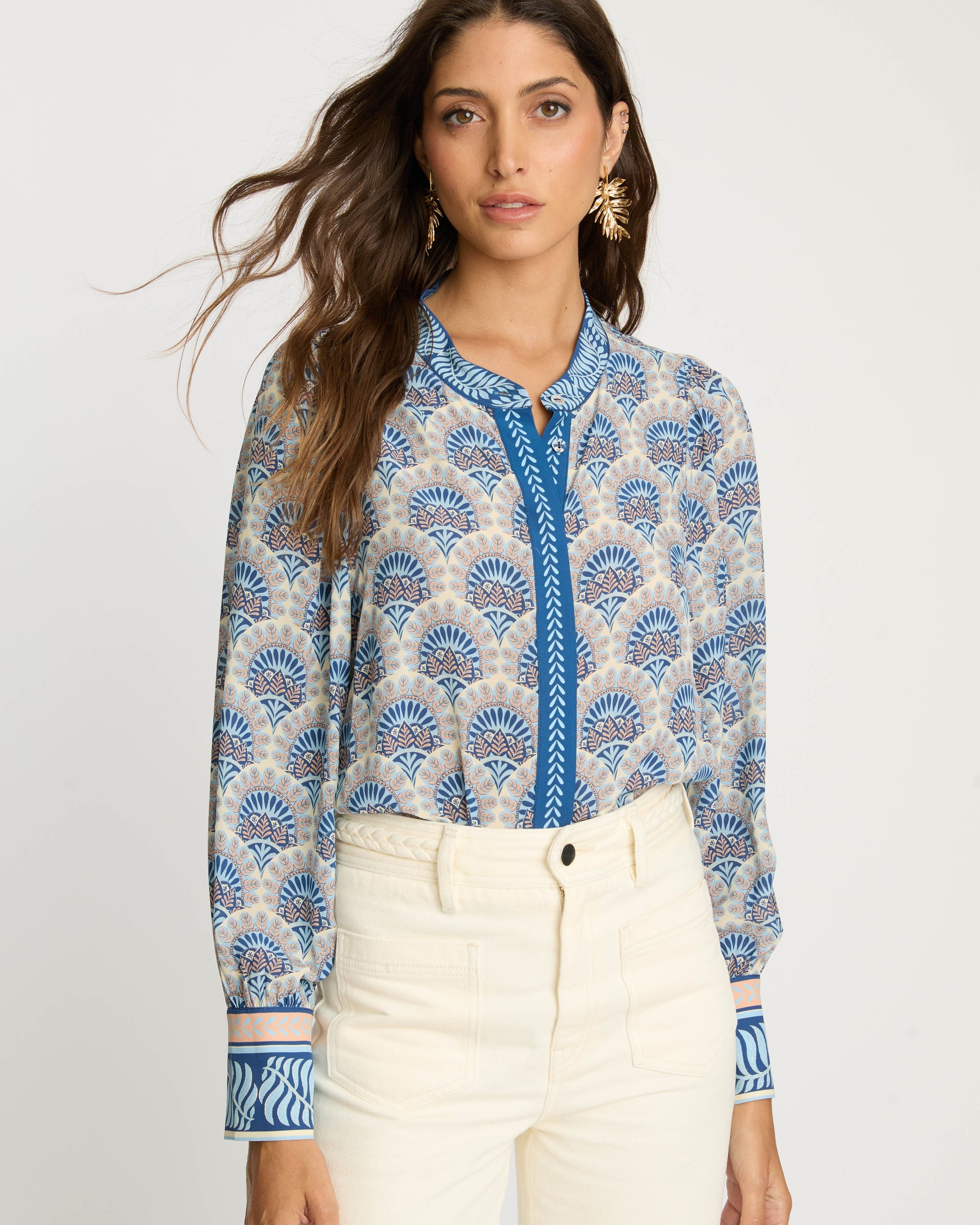 Woman wearing a blue patterned shirt and white pants on a light gray background