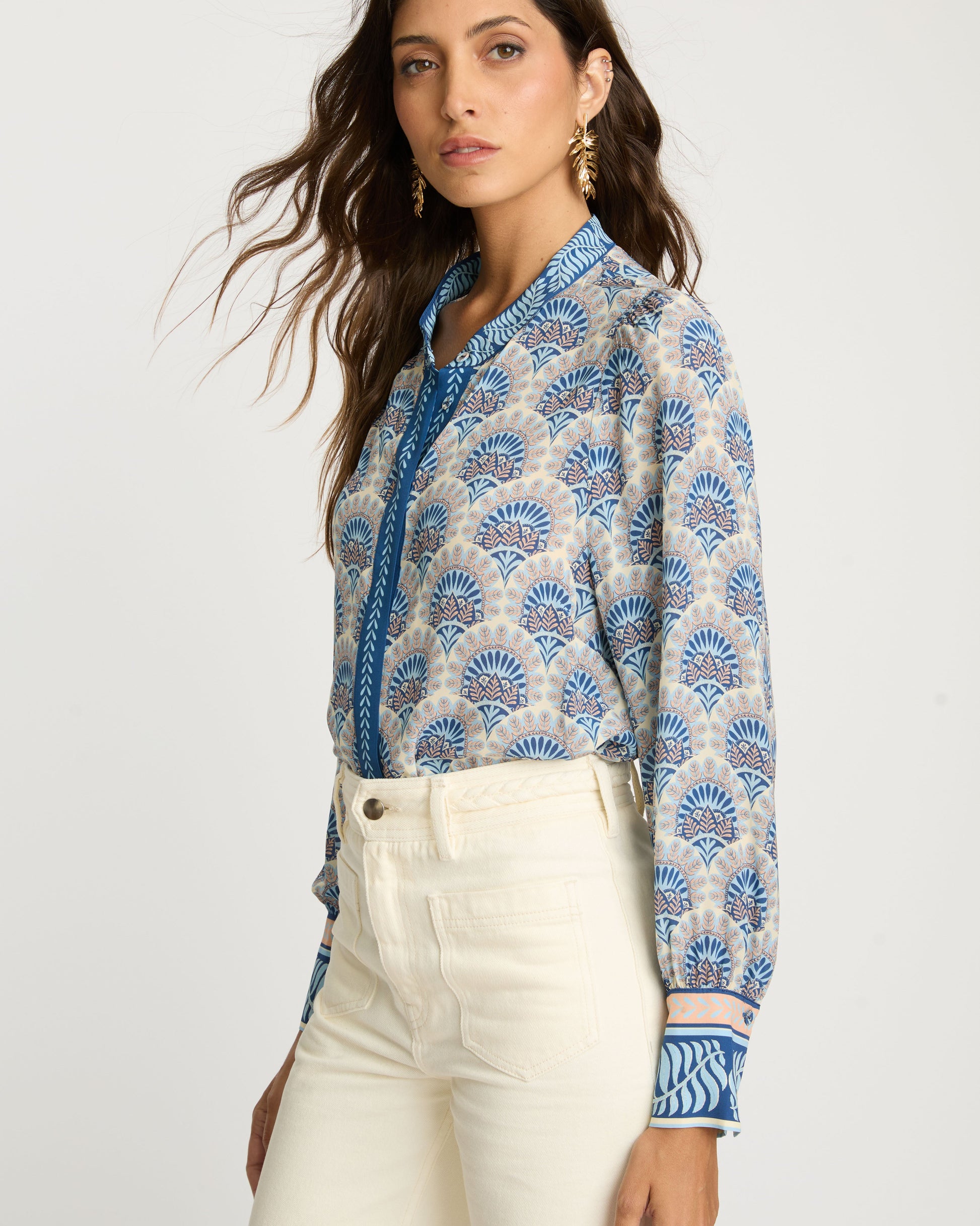 Woman wearing a patterned shirt with blue accents and white pants on a plain background