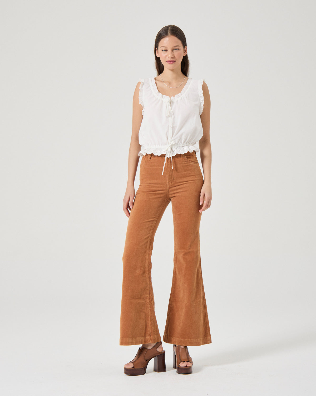 Woman wearing a white sleeveless top and brown flared pants on a white background