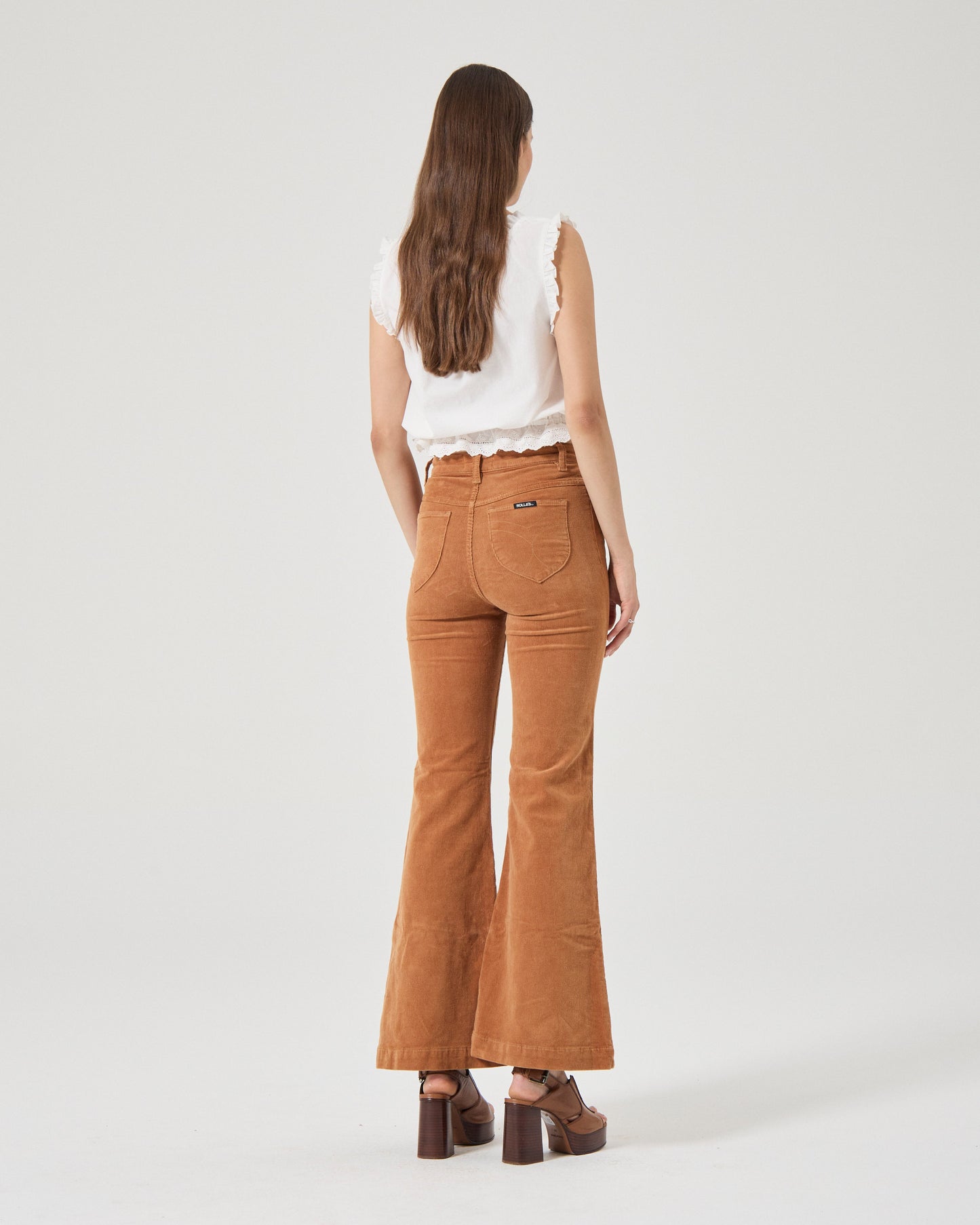 Woman wearing brown flared jeans and a white top on a white background