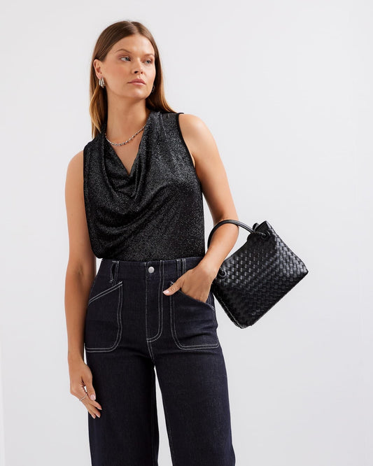 Woman wearing a black sleeveless top and jeans, holding a black handbag against a white background