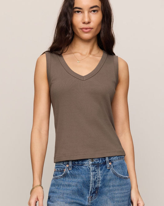 Woman wearing a brown tank top and blue jeans against a beige background