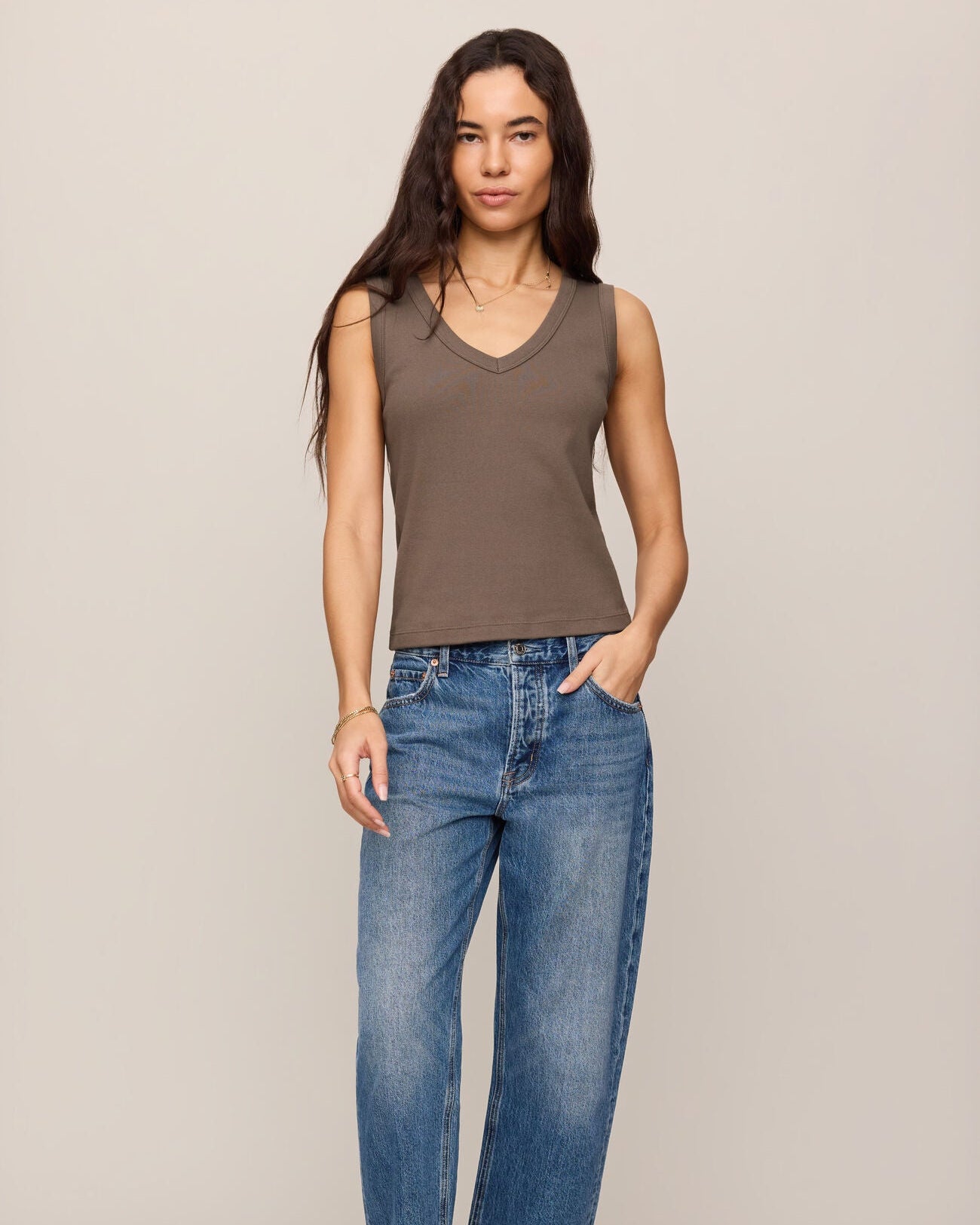 Woman wearing a brown tank top and blue jeans against a beige background