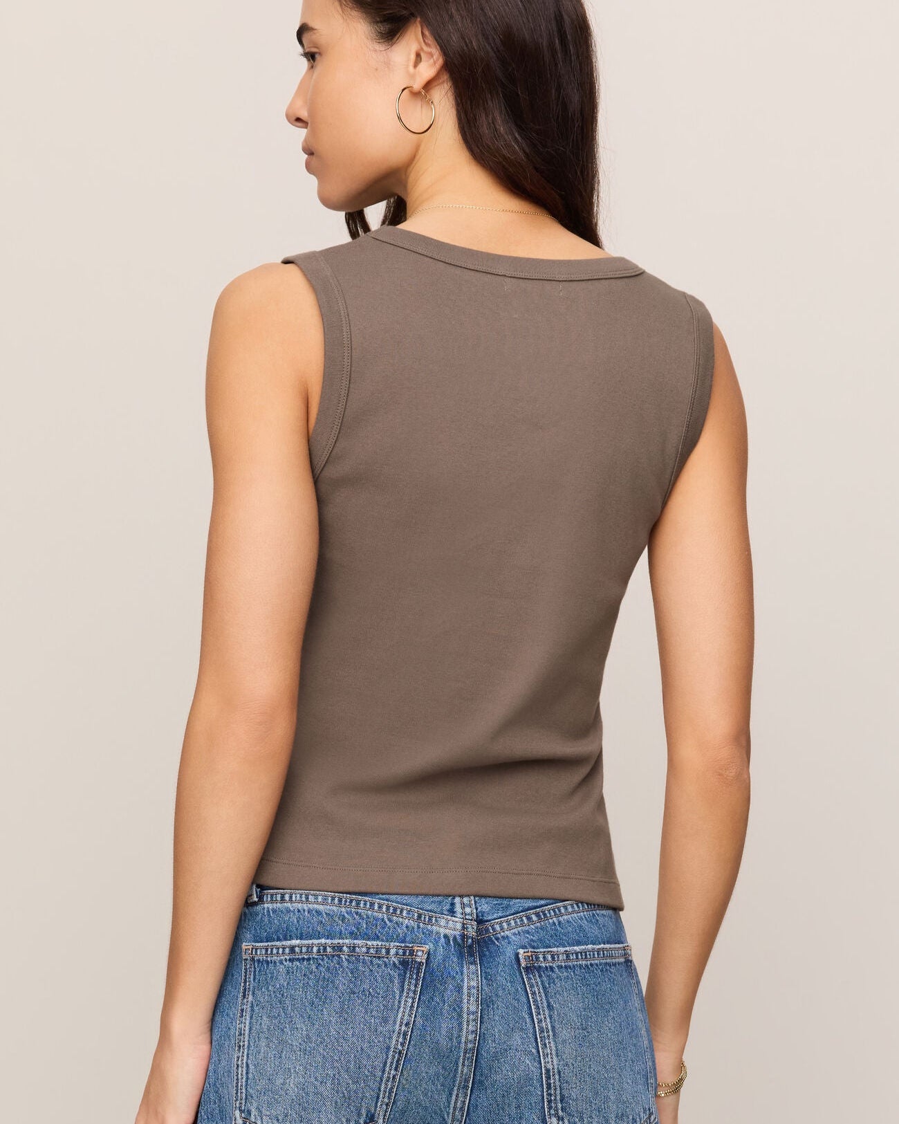 Woman wearing a brown sleeveless top and blue jeans against a beige background