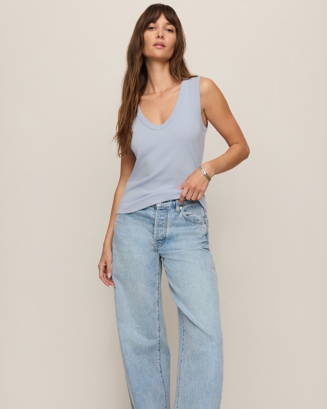 Woman wearing a light blue sleeveless top and jeans on a plain background
