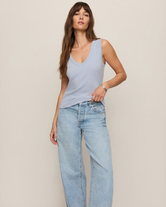 Woman wearing a light blue sleeveless top and jeans on a plain background