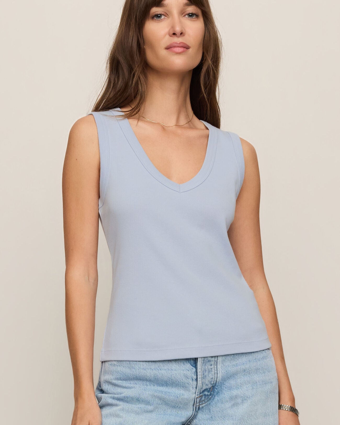 Woman wearing a light blue sleeveless top and jeans on a beige background