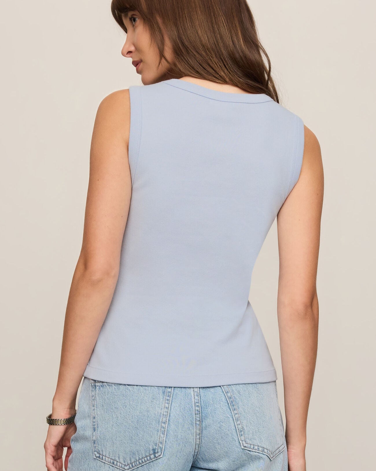 Woman wearing a light blue sleeveless top and jeans on a beige background