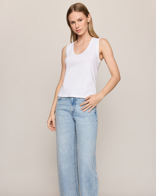 Woman wearing a white tank top and light blue jeans against a plain background