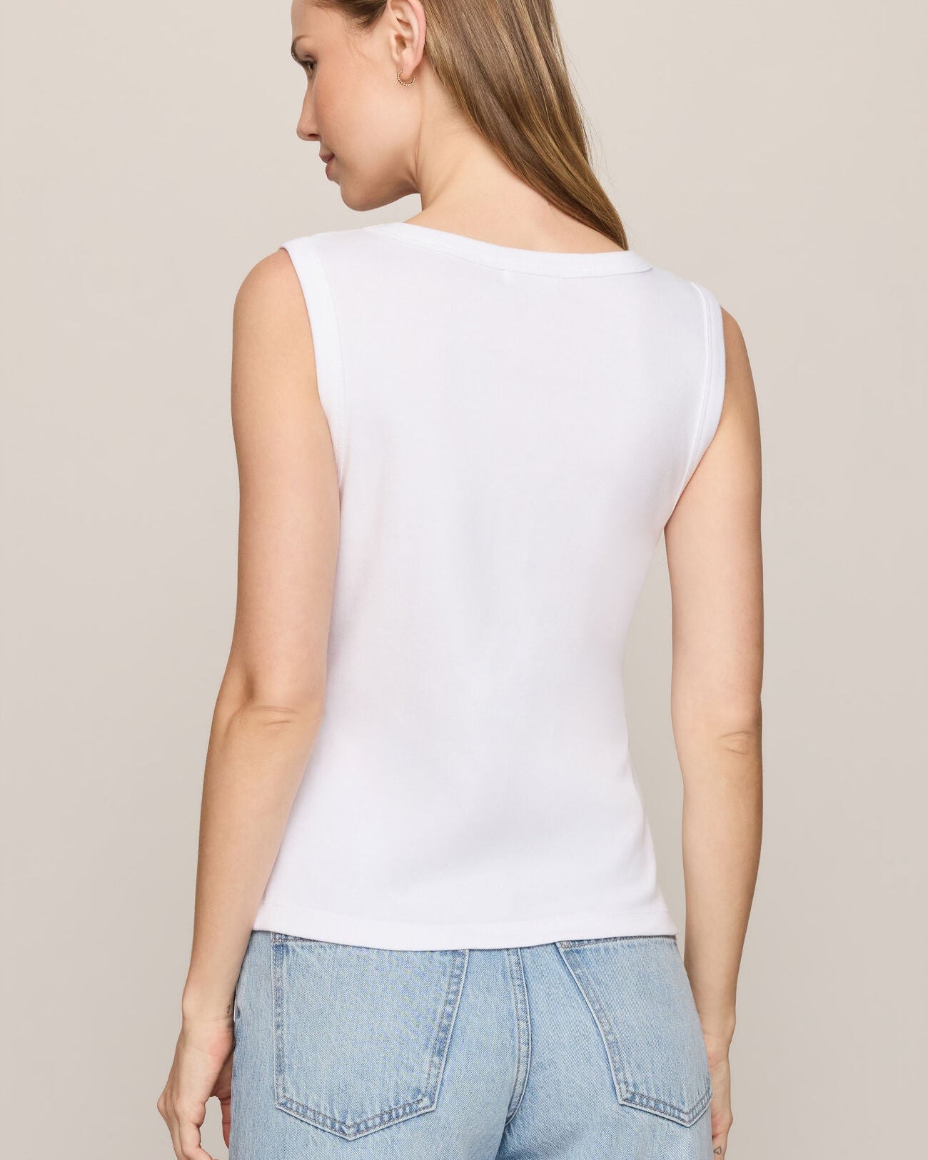 Woman wearing a white sleeveless top and light blue jeans on a beige background