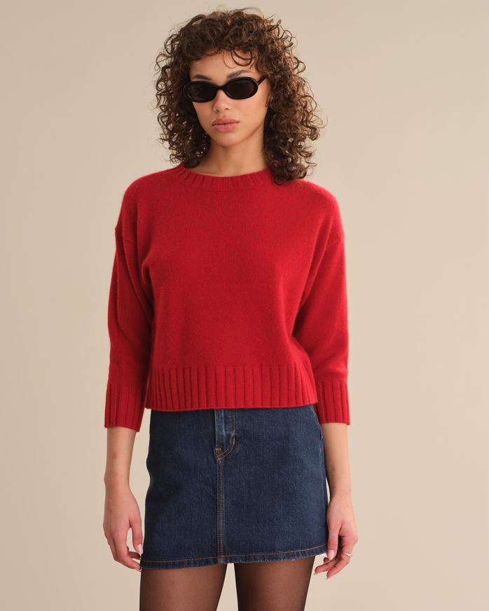 Woman wearing a red sweater and blue denim skirt against a beige background