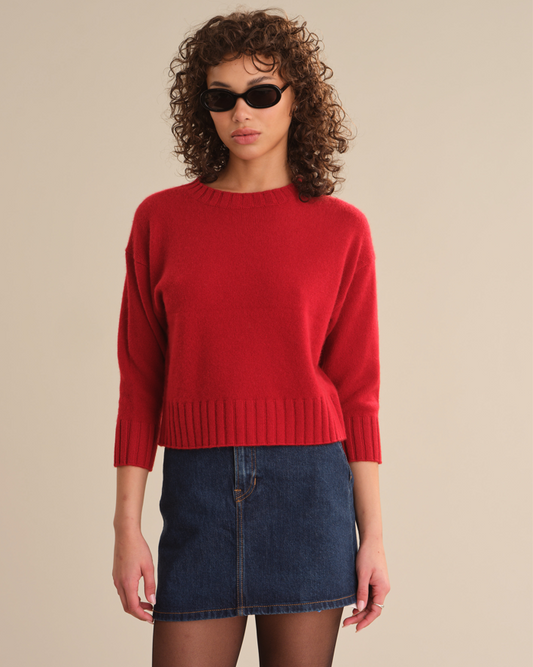 Woman wearing a red sweater and blue denim skirt against a beige background
