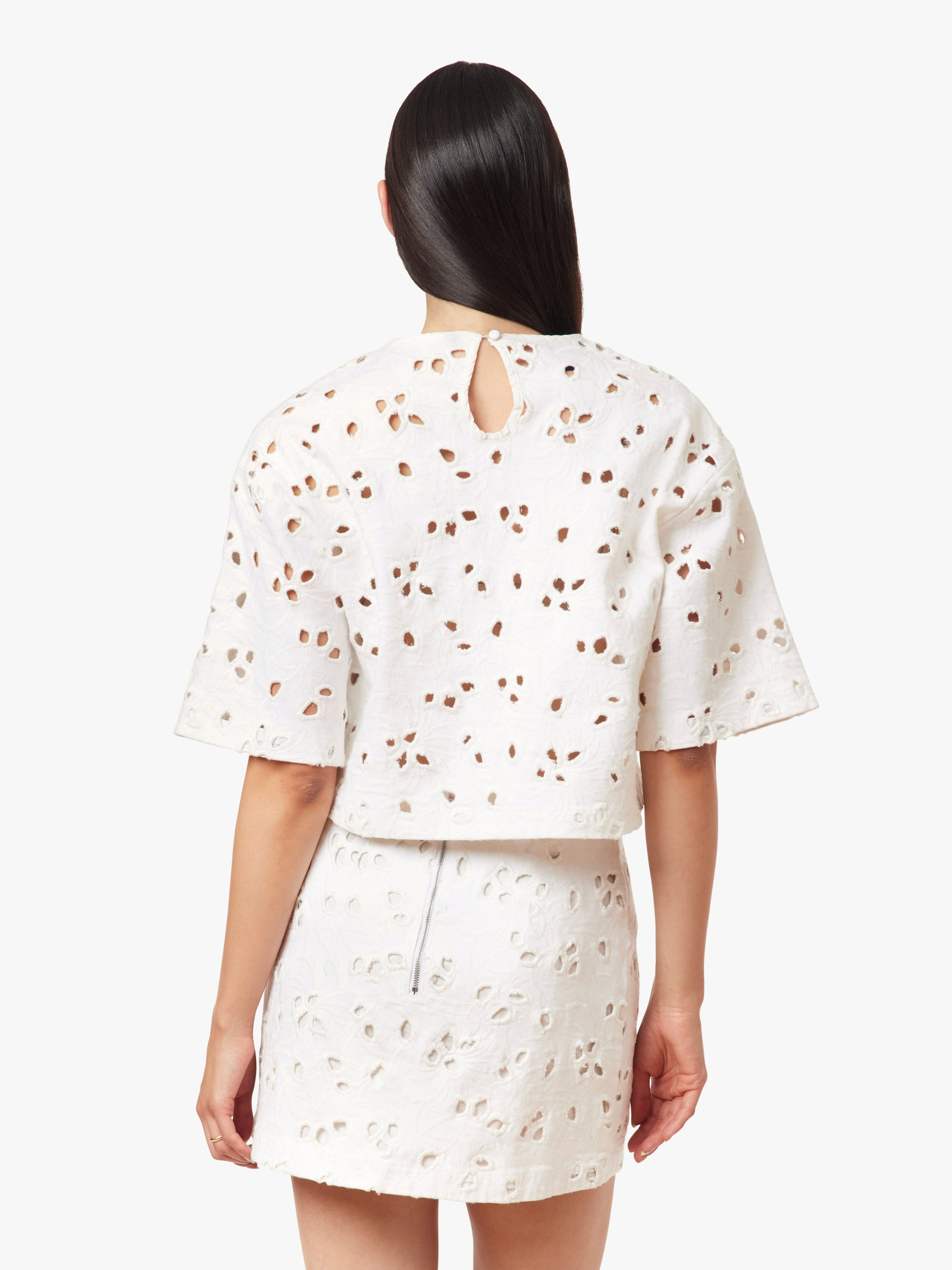 Person wearing a white outfit with small patterns on a plain background