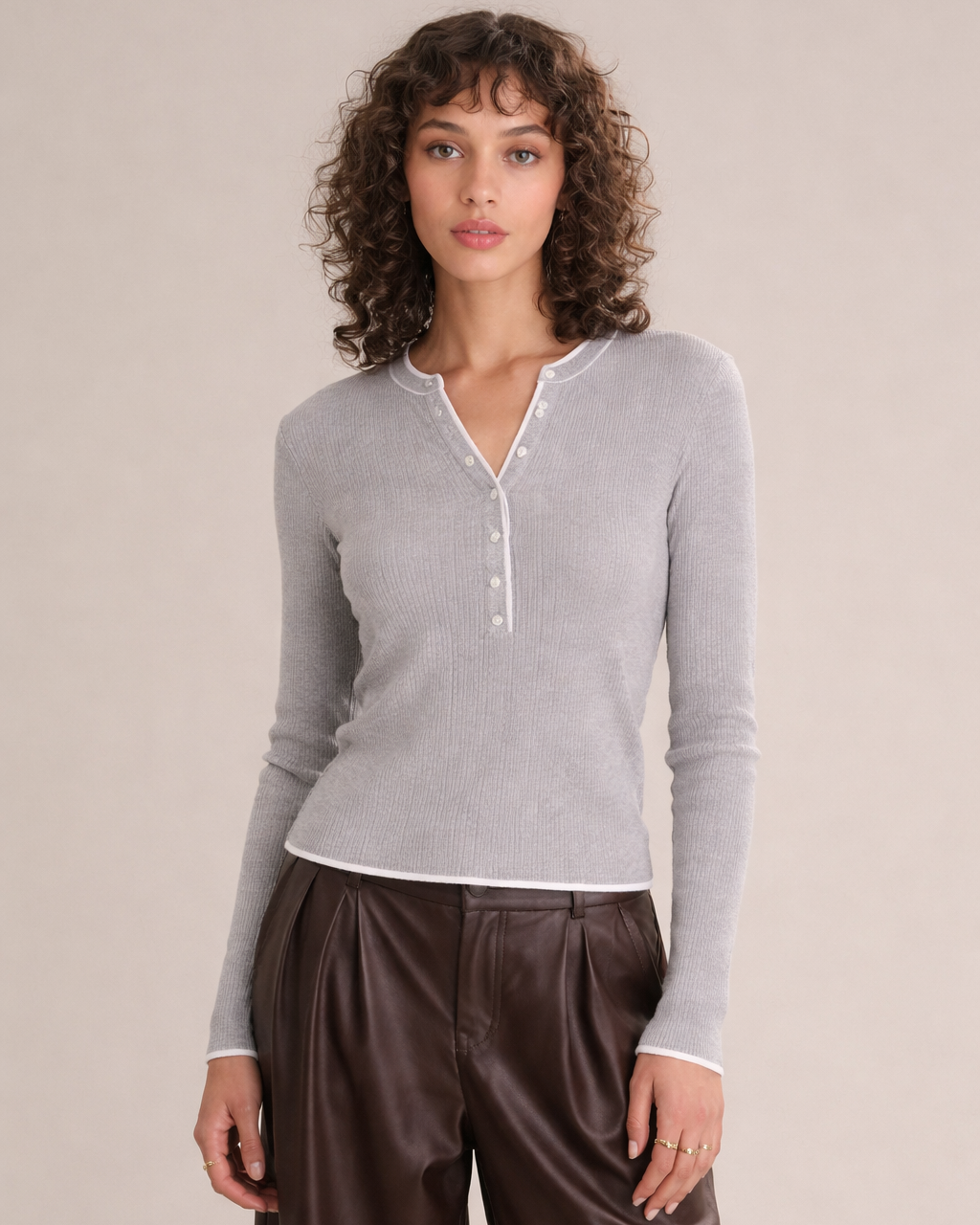 Woman wearing a gray long-sleeve shirt and brown pants against a beige background