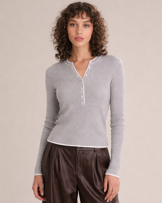 Woman wearing a gray long-sleeve shirt and brown pants against a beige background