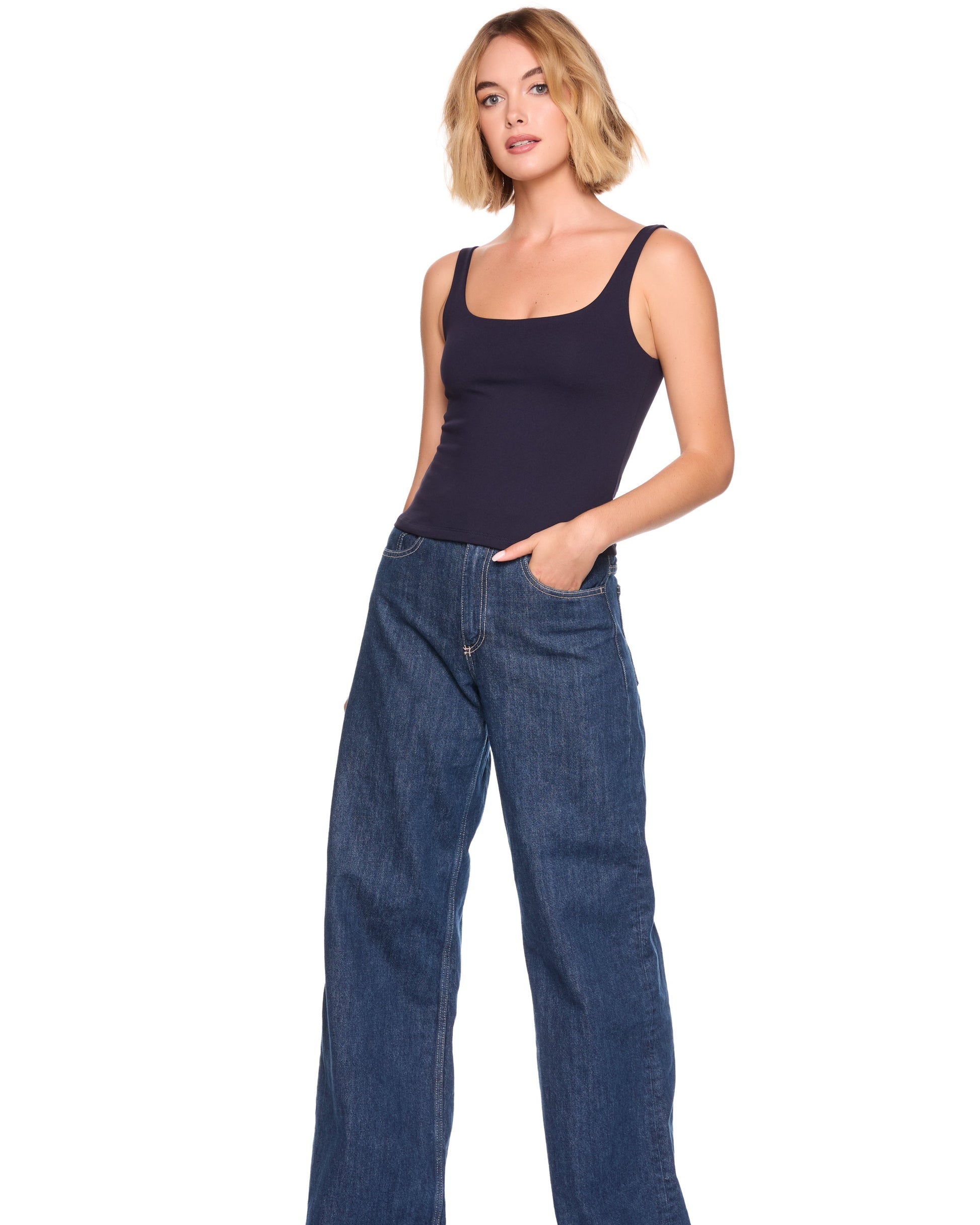 Woman wearing a navy tank top and blue jeans on a white background