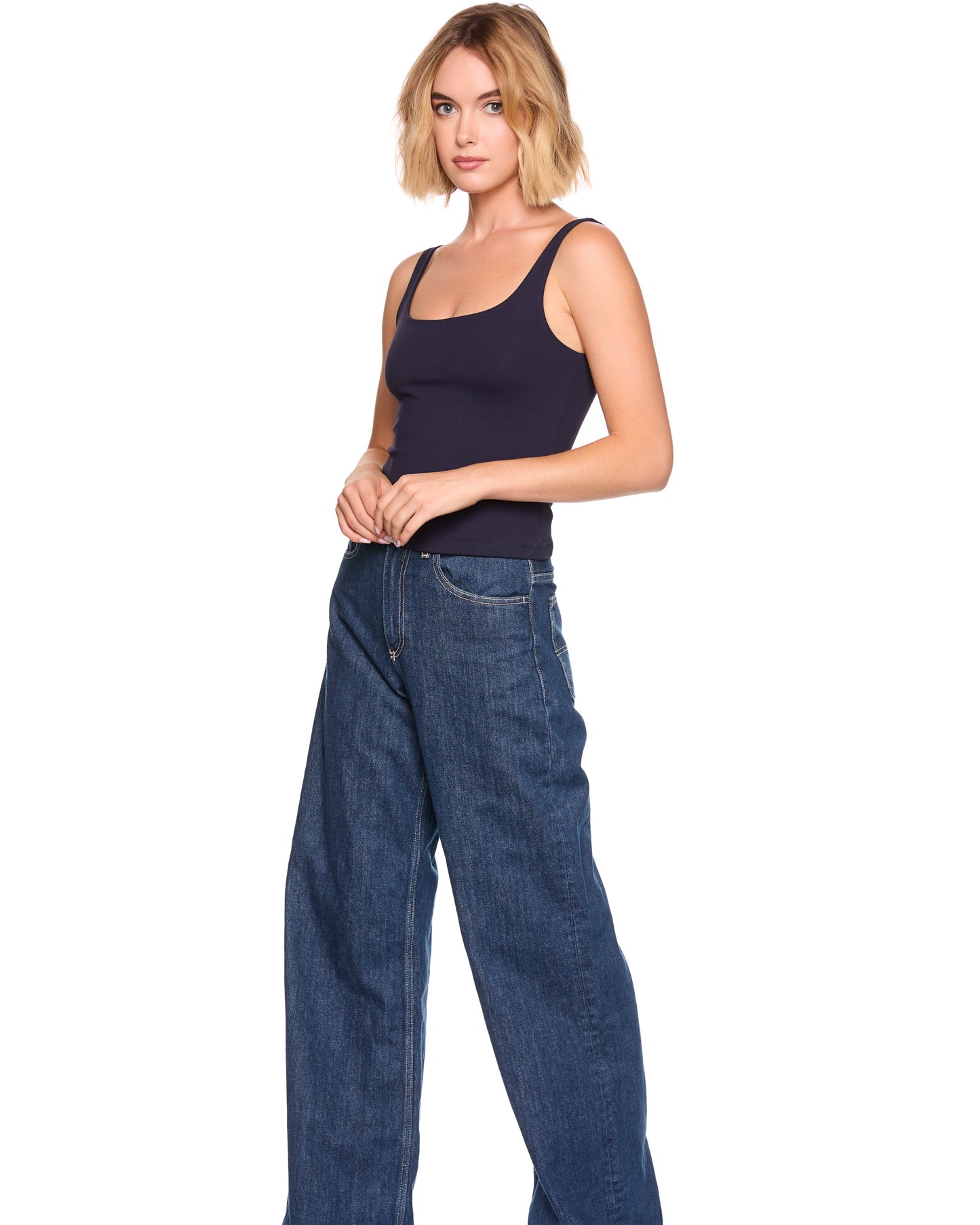 Woman wearing a navy tank top and blue jeans on a white background