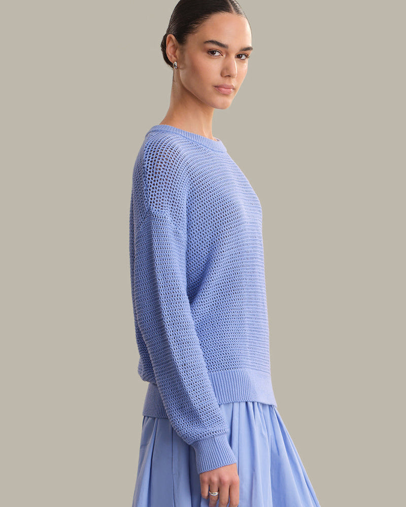 Woman wearing a light blue knitted sweater and skirt against a neutral background