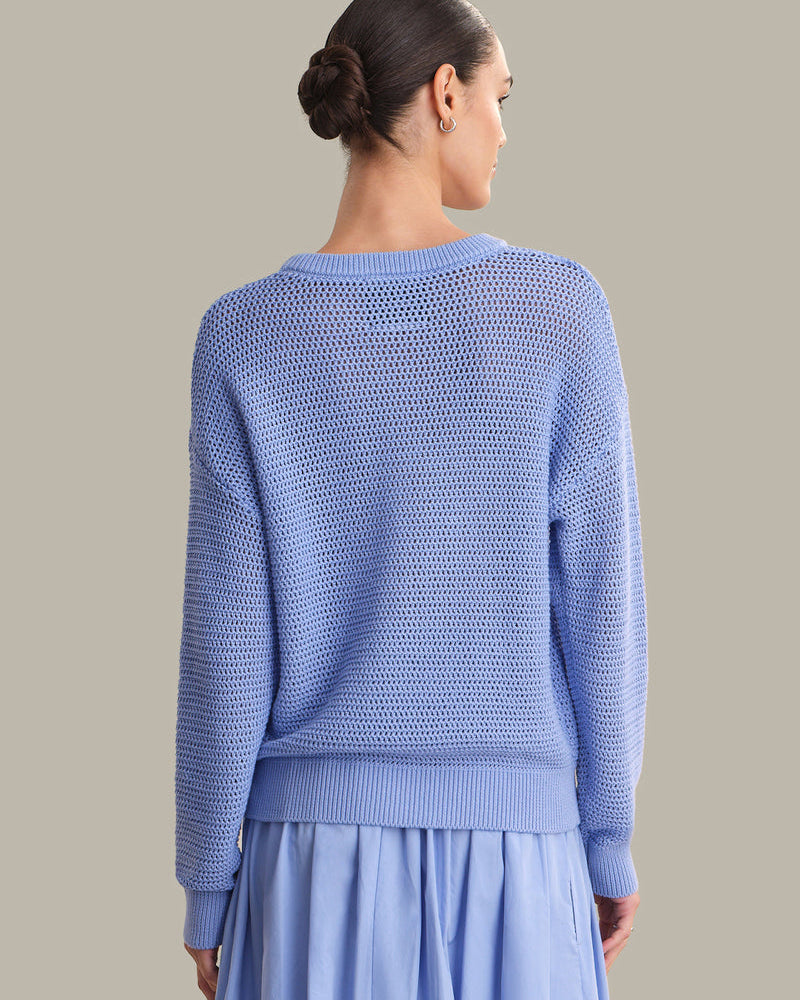 Woman wearing a light blue knitted sweater and skirt against a neutral background