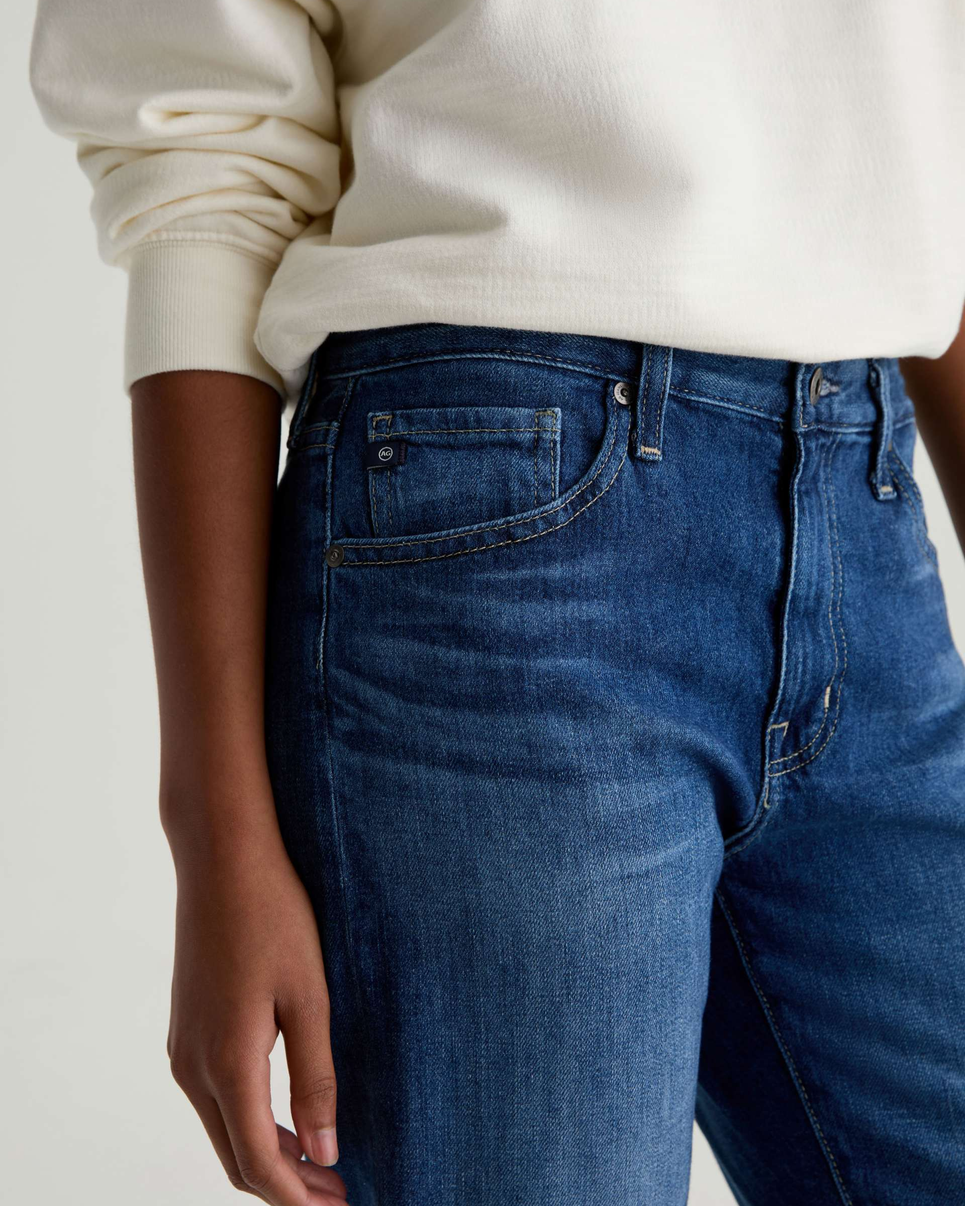 Person wearing blue jeans and a white sweater on a plain background