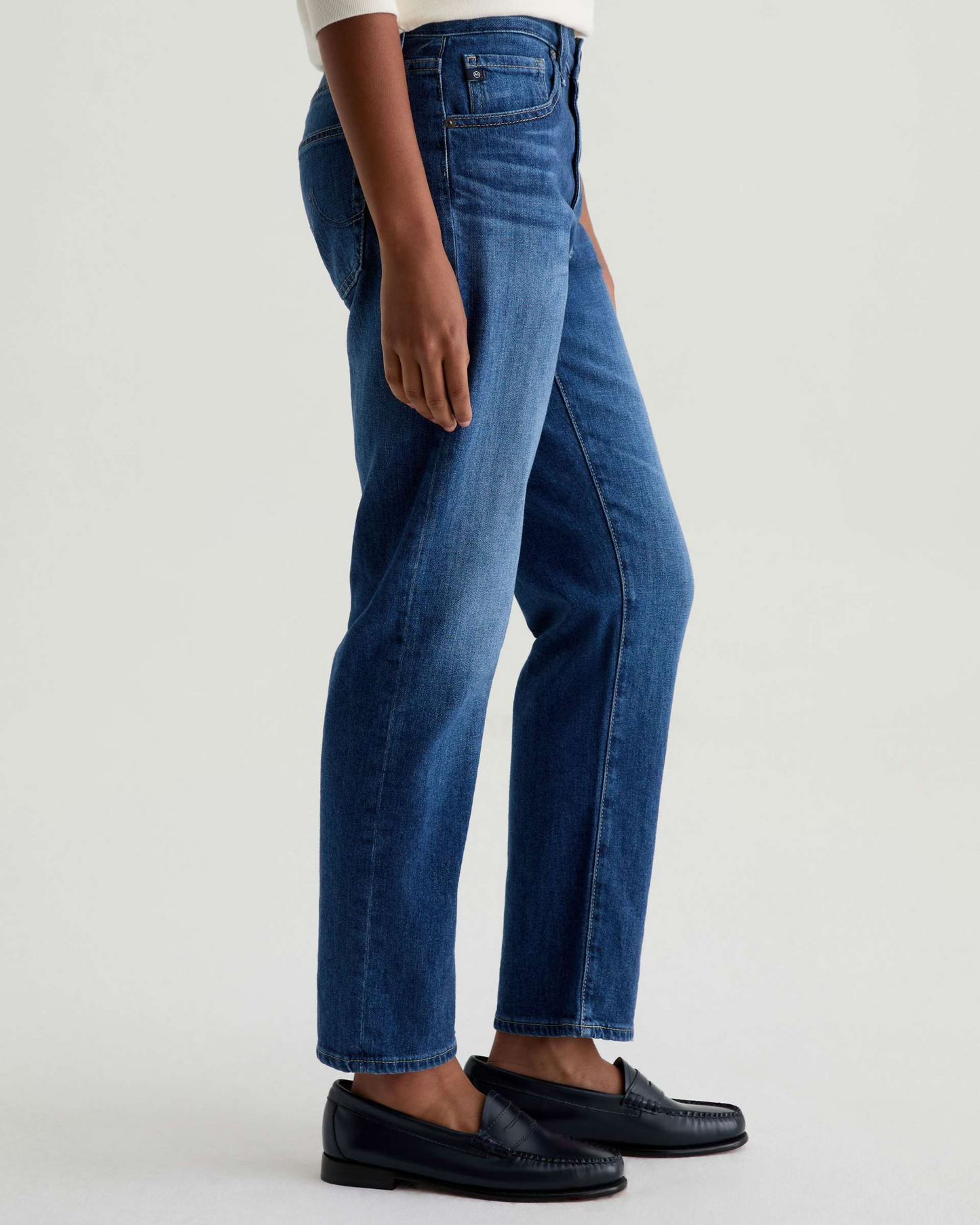 Person wearing blue jeans and black shoes on a white background
