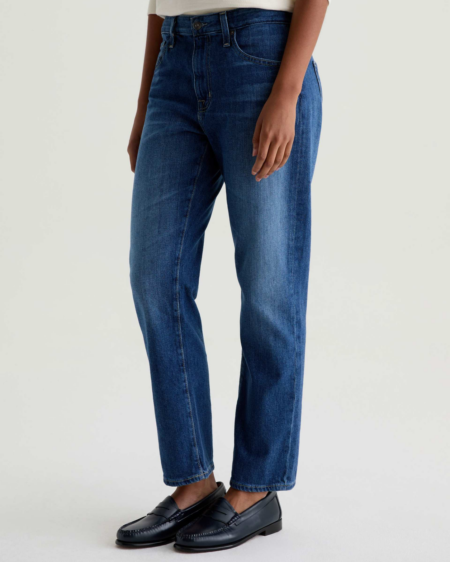 Person wearing blue jeans and black shoes on a white background